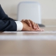 Man in an elegant suit put his hands on a wooden table next to a sheet of paper and a fountain pen. Without a face. Anonymous meeting participant: boss, official, lawyer, or businessman. Close-up