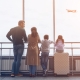 Full length of family with two little kids looking at the flying airplane while standing in airport terminal