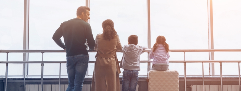 Full length of family with two little kids looking at the flying airplane while standing in airport terminal