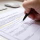 Close up of a female hand filling out a visa application document, white table with computer keyboard and a mouse in background