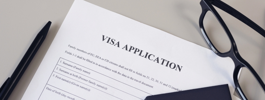 Visa application form, pen, eye glasses and passport on desk.