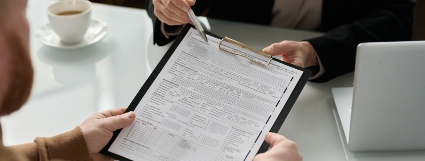 Closeup of insurance advisor handing application form to client during consultation